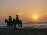 Two People on Horseback Ride Along an Ocean Shoreline at Sunset