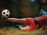 A Man Bends Sideways as He Kicks a Soccerball