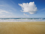 A Large Cloud Dominates the Sky as the Surf Rolls onto a Sandy Beach
