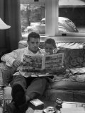 Father Sitting on Couch with Pigtailed Daughter Reading to Her the Sunday Comic Pages