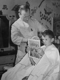 12 Year Old Boy Sitting in Barber Chair Having His Hair Cut and Reading Comics
