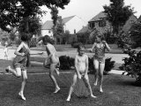 Four Children in Bathing Suits Playing with Water Sprinkler and Running Through Spray on Front Lawn