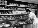 Good of Worker in Bakery Standing in Front of Shelves of Various Kinds of Breads and Rolls