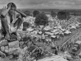 Boy Sitting on Rock Ledge Above Refugee Camp