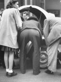 View of the Backsides of Two Men Leaning over Looking at a Small Sports Car