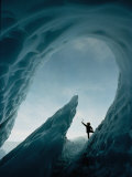 A Climber Raises His Ax in Triumph Near the Opening of an Ice Cave