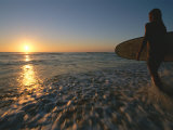 A Woman Enters the Ocean with a Surfboard under Her Arm
