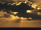 Rays of Sunlight Beam from Behind a Dark Cloud over Water at Twilight