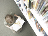 Little Boy Reading Book Beside Library Shelf