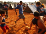 Children Play Soccer Between Tents Placed on a Dusty Lot