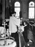Priest sprinkling Holy Water on baby held by woman in front of altar in Ukrainian Orthodox Church