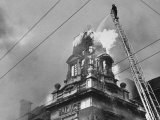Fireman on Ladder Using a Hose to Extinguish Blazing Building Set Afire