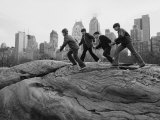 Boys Climbing About on Rock Formation in Central Park as Essex House Looms Amidst Skyline of City