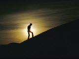 Silhouette of a Man Walking up a Dune against a Cloudy Sun