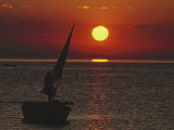 A Windsurfer Comes Near a Small Boat at Sunset