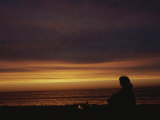 Woman Sitting by Campfire on the Beach at Sunset