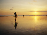 A Surfer with a Surfboard in Hand Walks Toward the Ocean at Sunset