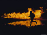 A Silhouetted Man Runs Past a Wall of Fire and its Reflection at Night