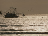 A Silhouetted Fishing Boat Hauls in a Net on a Silvery Sea