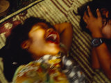 Two Young Girls Laugh Hysterically on a Bamboo Straw Mat in a Park