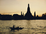 A Man Paddles a Boat Past Wat Arun at Twilight