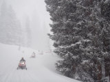 A Small Group of Snowmobilers Turn a Corner in a Snowstorm