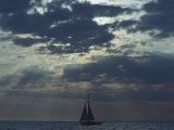 Sunlight Breaks Through a Cloudy Sky onto a Sailboat at Sea