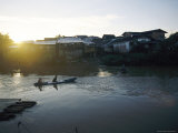 The Sun Sets Behind Waterfront Housing as People Paddle a Canoe Back Home