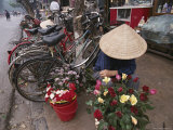 A Flower Vendor Sitting on a Sidewalk Next to a Row of Parked Bicycles