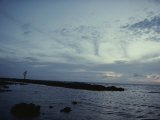A Silhouetted Person Walks Down a Jetty at Twilight