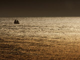 A Sailing Ship Crosses Waters Turned Gold by the Setting Sun