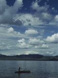 A Man Rows a Boat to Shore under a Cloud-Filled Sky