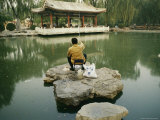 Man Fishes in a Green Pond Surrounded by Chinese Architecture