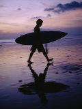 A Surfer Walks Along Kuta Beach at Dusk with His Surfboard in Hand