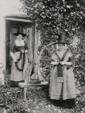 Two Welshwomen in Traditional Dress Stand Outside Their Cottage with a Spinning Wheel