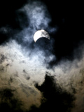 The Moon Partially Covers the Sun Behind the Clouds During a Partial Solar Eclipse