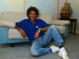David Essex  Sitting on the Floor Leaning Against a Sofa Wearing Denim Jeans and Blue Top
