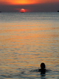 Sun Setting over Sea with Silhouette of Person Swimming
