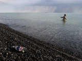 Man Swimming in Lake Alakol with Vodka Bottle Lying on Black Pebbled Beach in Foreground