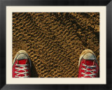 Red sneakers on soil patterned with tire tracks