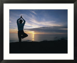 A woman practices yoga on the beach at sunset