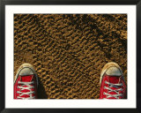 Red sneakers on soil patterned with tire tracks