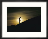 Silhouette of a man walking up a dune against a cloudy sun
