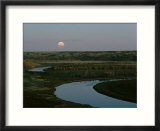 The moon rises over low hills banking the river
