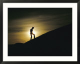 Silhouette of a man walking up a dune against a cloudy sun