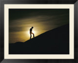 Silhouette of a man walking up a dune against a cloudy sun