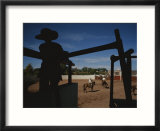 A silhouetted cowboy watches riders in a ring