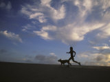 Woman and Her Dog Run Along the Beach with Beautiful Sky