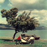 Two Young Women Moving a Boat Near a Large Tree on the Shore of a Lake
