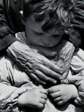 Child Dressed in a Preschool Pinafore with the Hands of an Elderly Woman Draped across His Chest